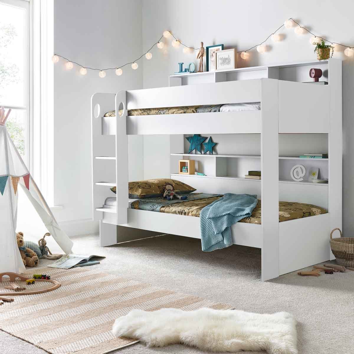 White wooden bunk bed with orthopaedic mattresses, featuring a ladder, open shelves, and a cozy room setting with fairy lights and a soft rug.