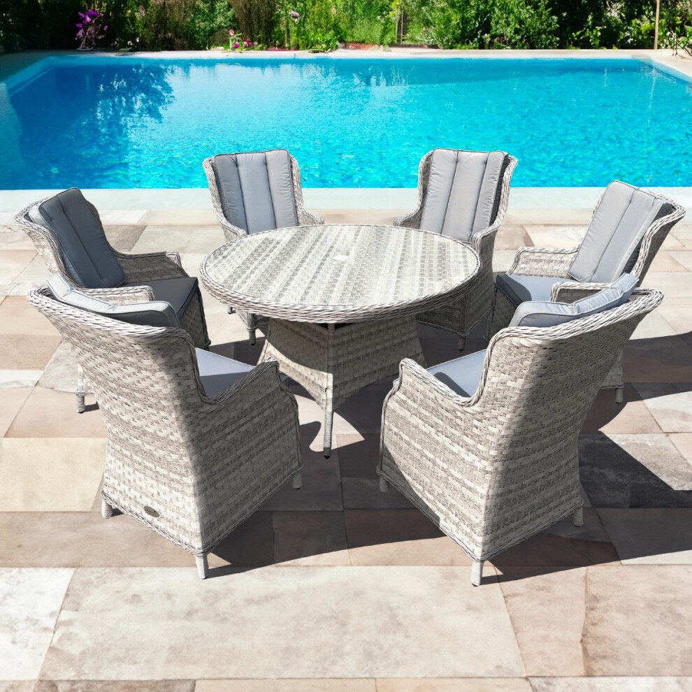 Knightsbridge XL rattan dining set featuring a 135cm round table in dove grey, accompanied by six cushioned chairs, set by a poolside with greenery in the background.