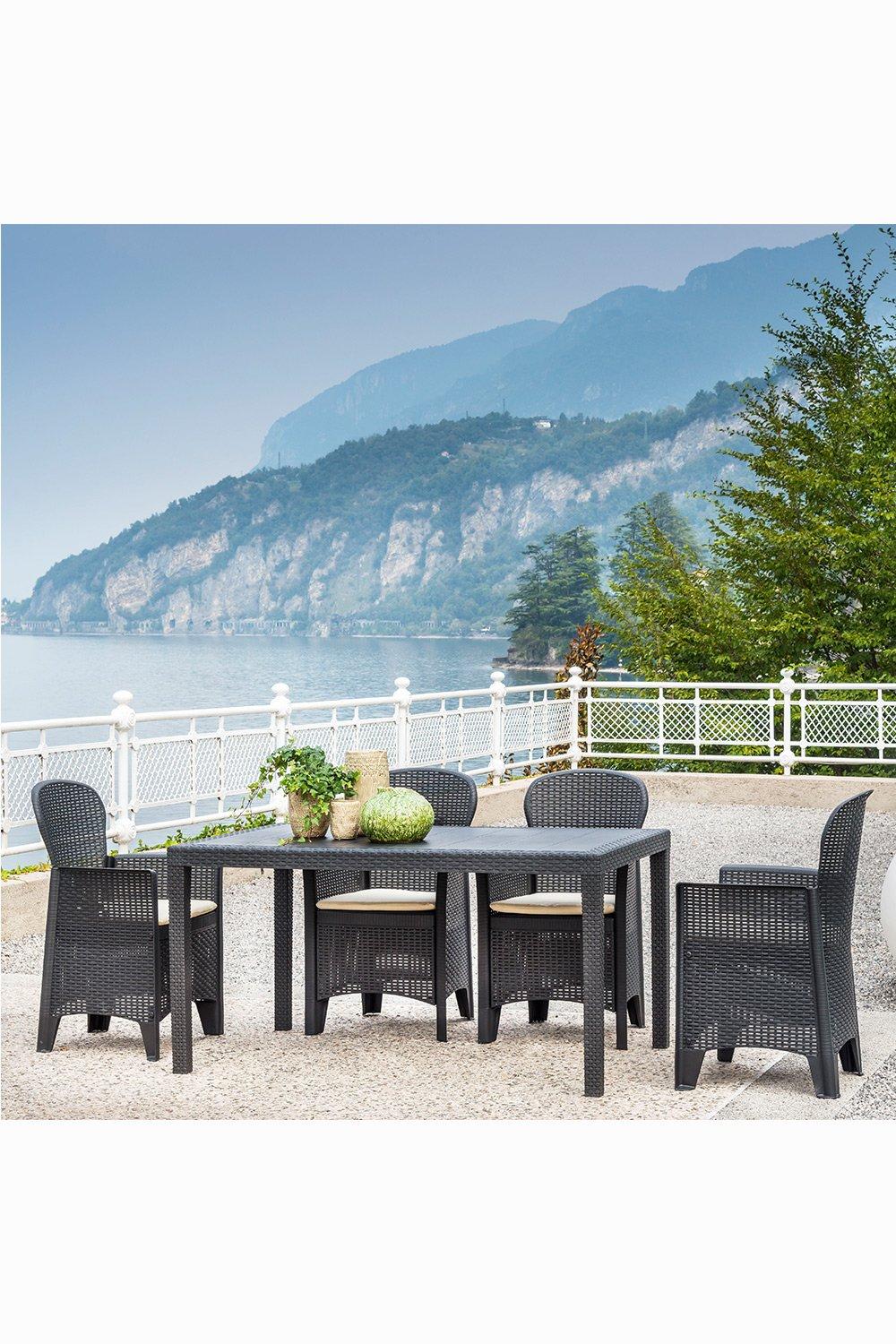 The Italian Campania 4 Seat Rattan Dining Set features a sleek dark grey rattan design with a rectangular table and four matching chairs, set against a scenic lakeside backdrop.