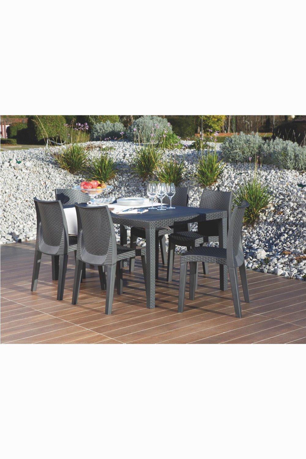 The Tuscany Italian 6 Seat Rattan Dining Set features a stylish black rattan table and six matching chairs, set on a wooden deck surrounded by greenery and gravel.