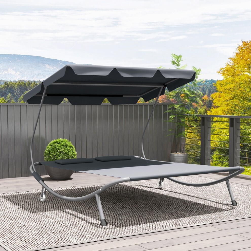 Grey double hammock sun lounger with a canopy and two pillows, featuring a sturdy metal frame and a sleek design, set on a textured outdoor rug against a scenic backdrop.