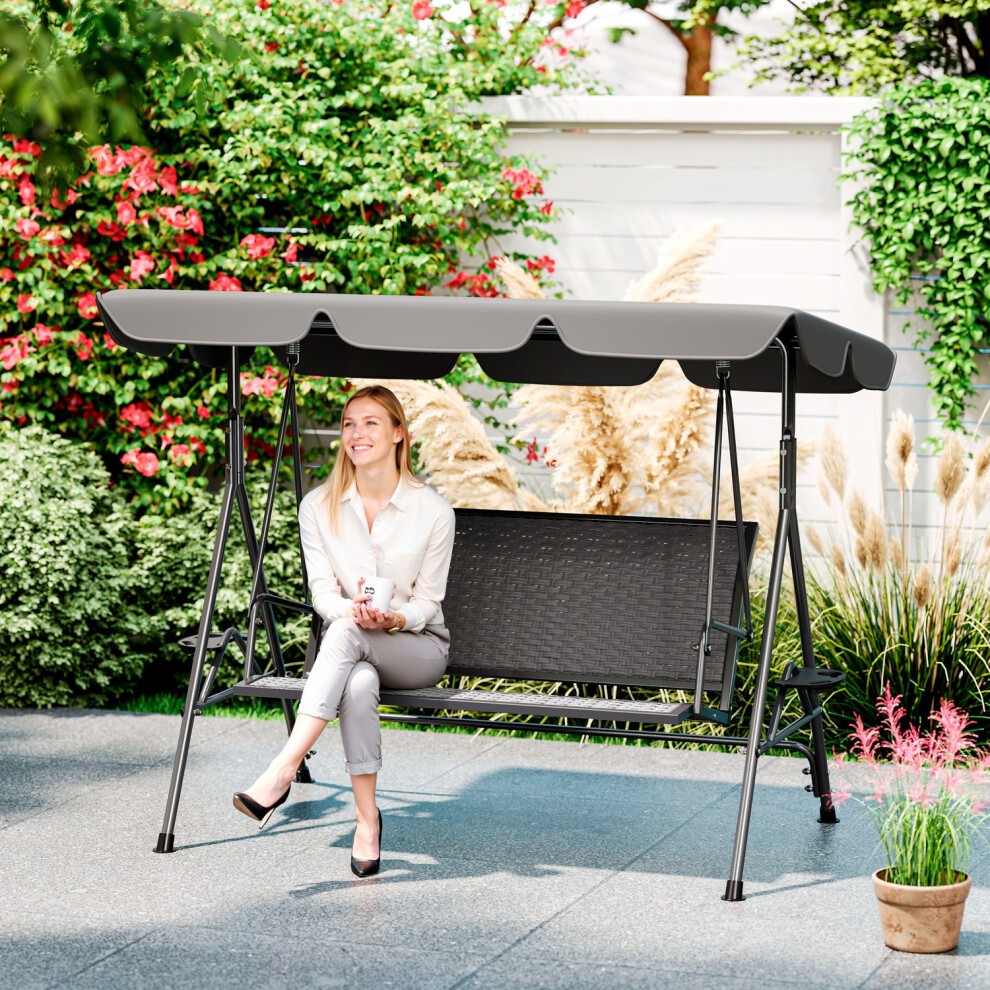 Grey 3-seater garden swing seat bench with an adjustable canopy, featuring a black woven seat and sturdy metal frame, set in a lush garden environment.