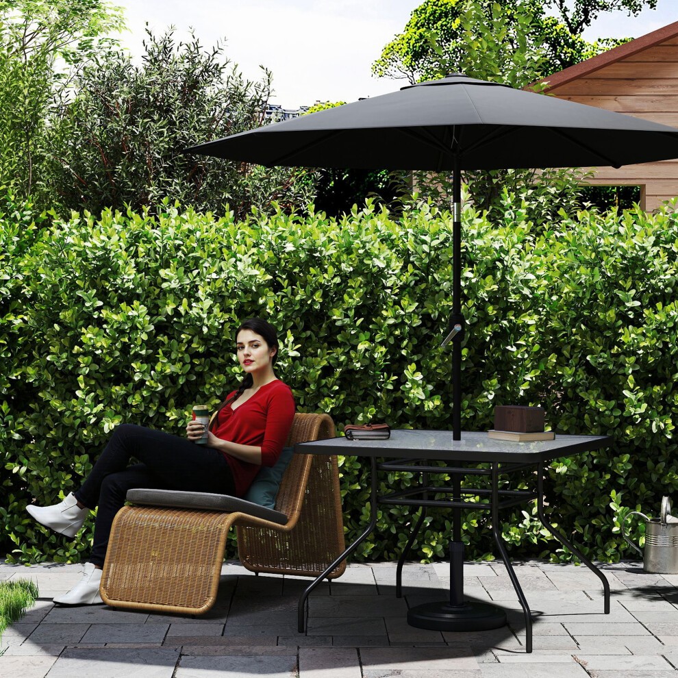 Square black patio table with a glass top, measuring 100 x 100 cm, set in a garden with a woman sitting beside it under a black umbrella, surrounded by lush greenery.