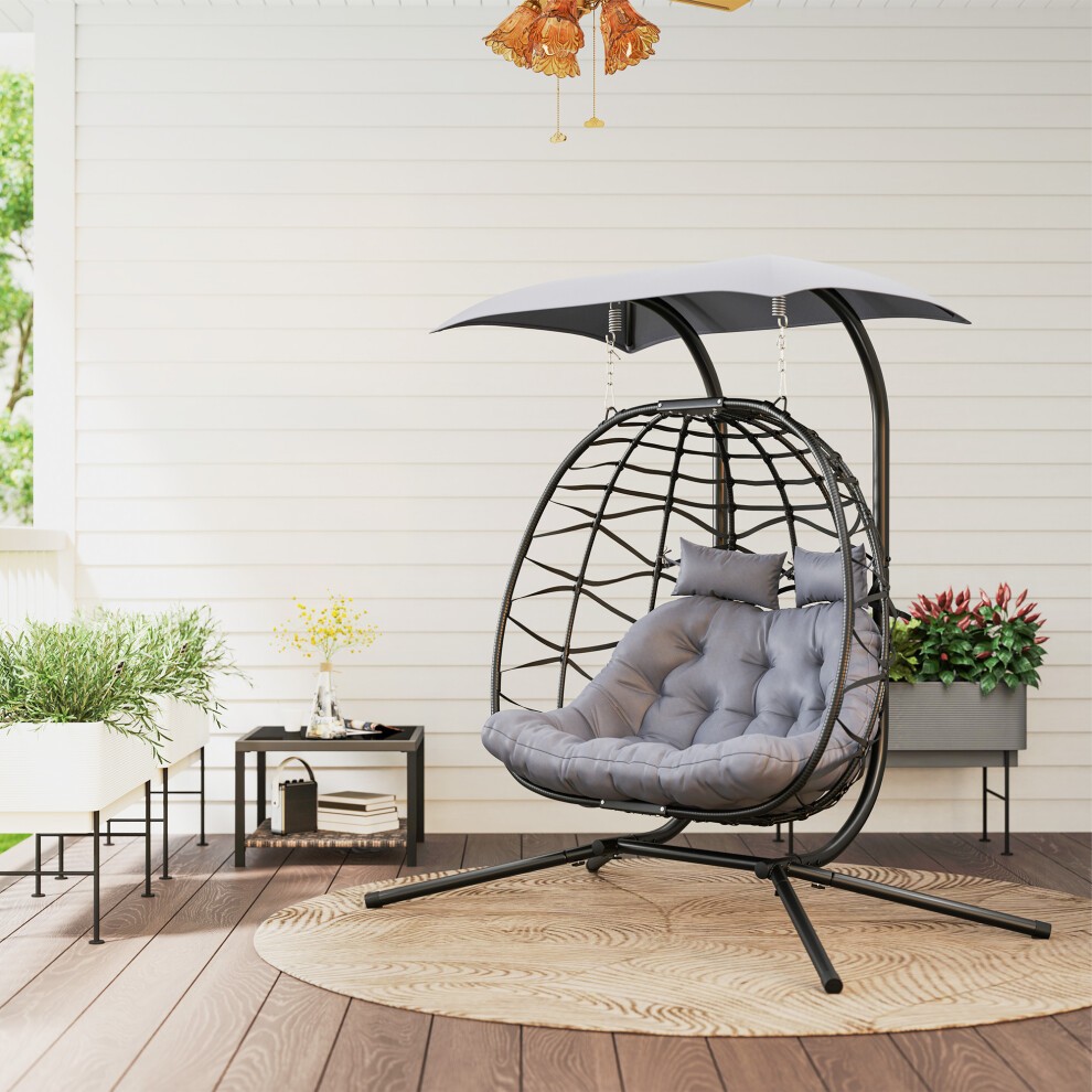 Rattan double hanging egg chair in black with a gray cushion and a canopy, featuring a sturdy metal frame and a stylish design, set on a wooden deck.