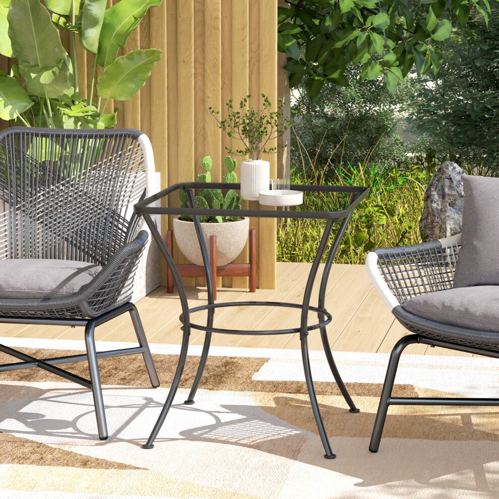 Black metal square bistro table with a sleek design, featuring a glass top and sturdy legs, set amidst outdoor seating and greenery.