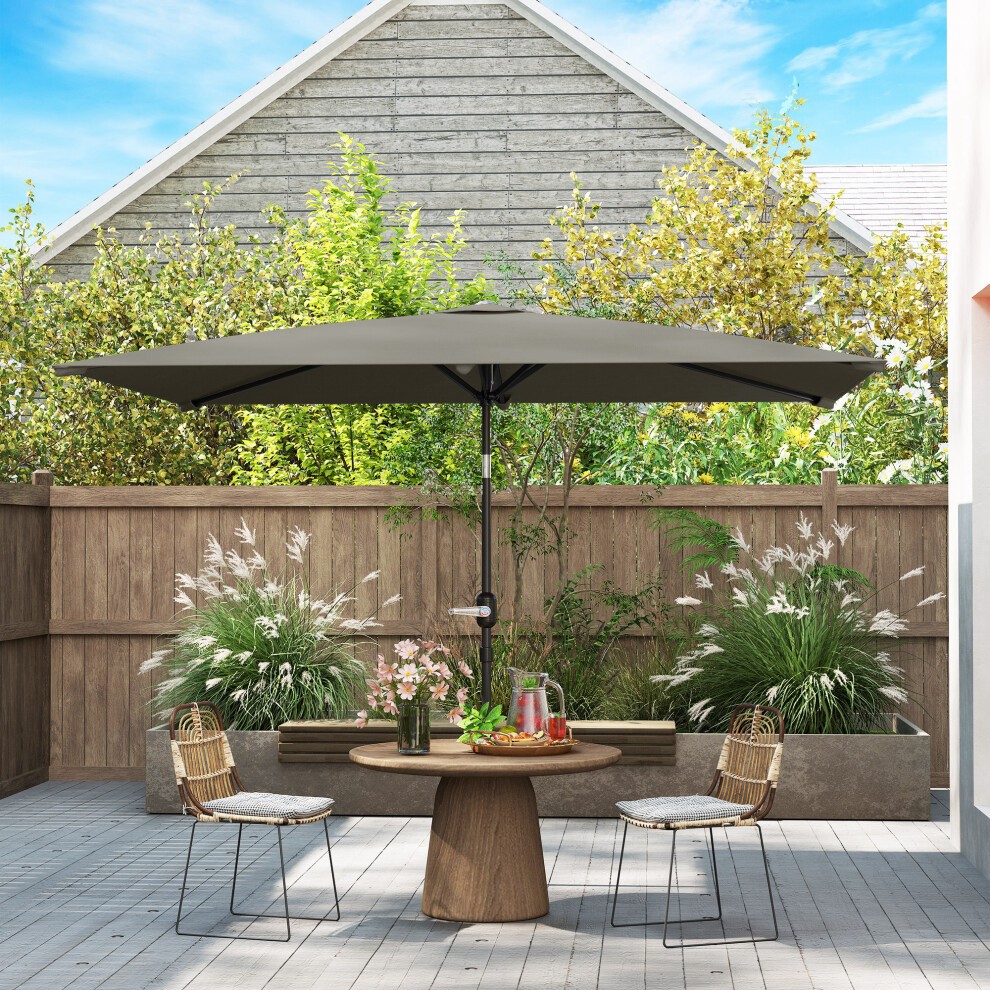 Light grey garden parasol with a tilt crank and six ribs, set over a round wooden table in a landscaped outdoor area with greenery and decorative plants.