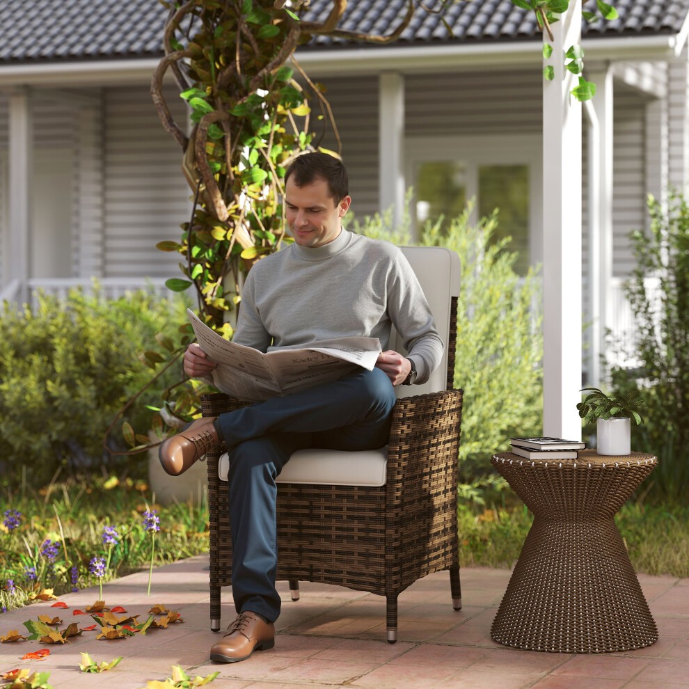 Cream rattan garden recliner chair with an adjustable backrest, featuring a woven design, paired with a round wicker side table, set in a leafy outdoor environment.
