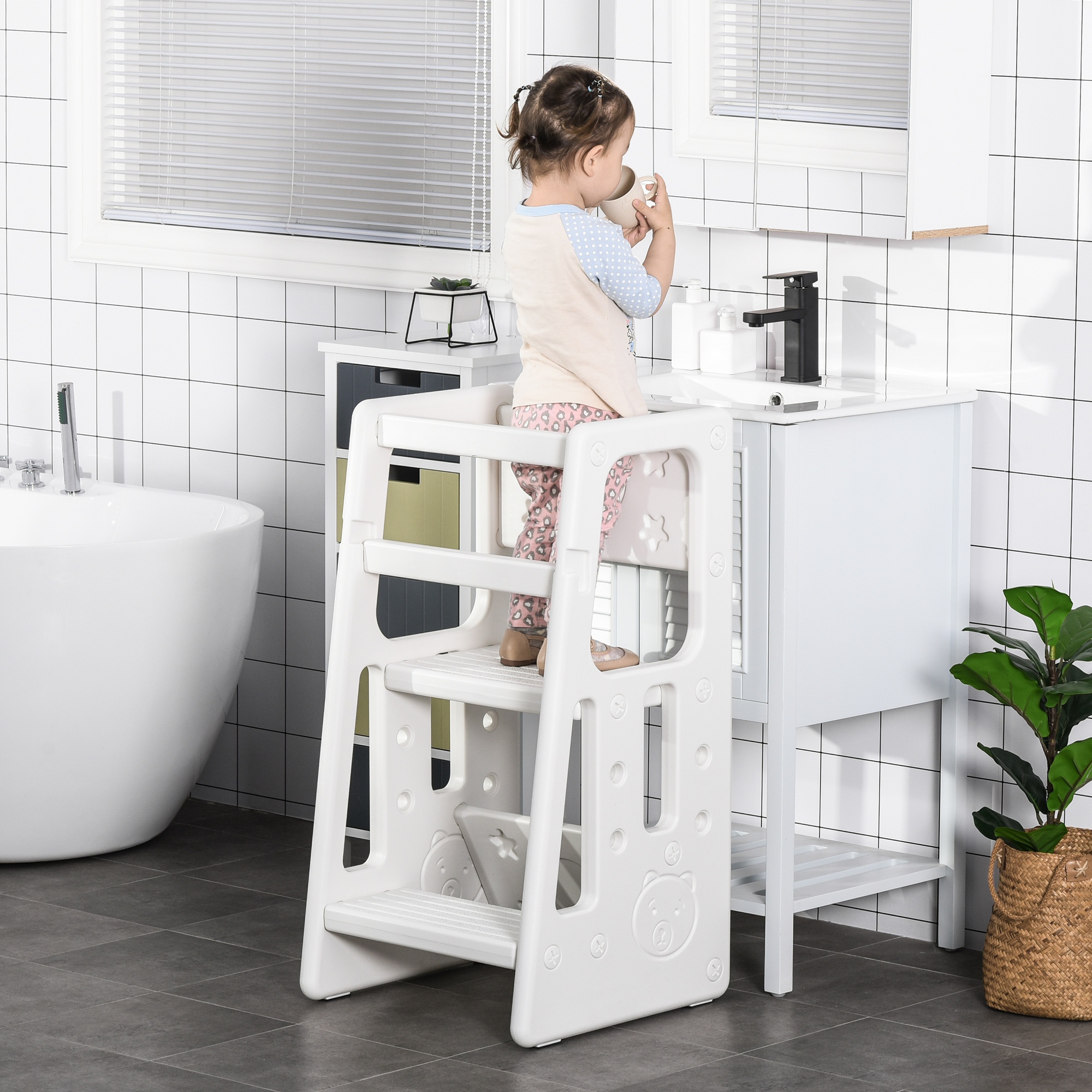 White adjustable kids step stool with three heights, featuring a sturdy design and playful cutouts, supporting a toddler standing at a bathroom sink.