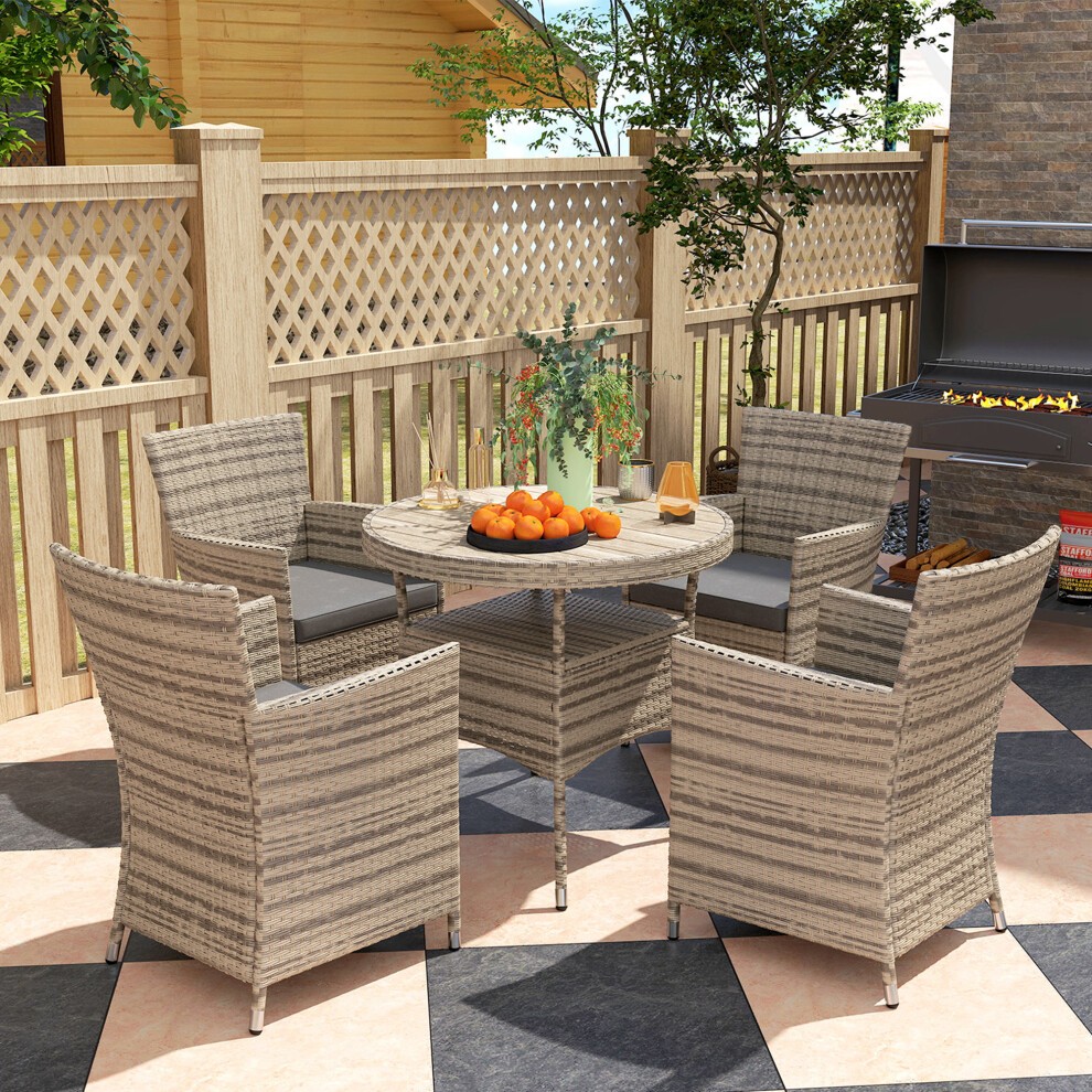 Grey rattan dining set for four, featuring cushioned chairs and a round table, set on a patterned patio with a wooden fence and greenery in the background.