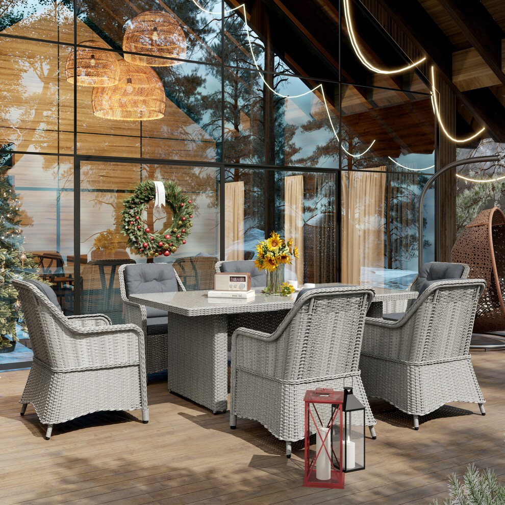 Grey rattan dining set for six, featuring a glass top table and cushioned chairs, set in a stylish outdoor space with wooden accents and decorative lighting.