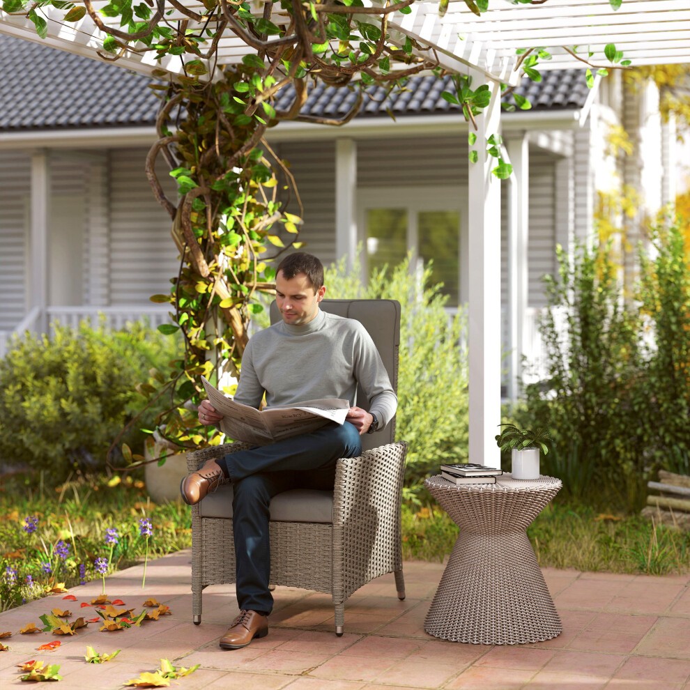 Grey rattan garden recliner chair with an adjustable backrest, featuring a man reading a newspaper beside a small woven side table in a landscaped outdoor setting.