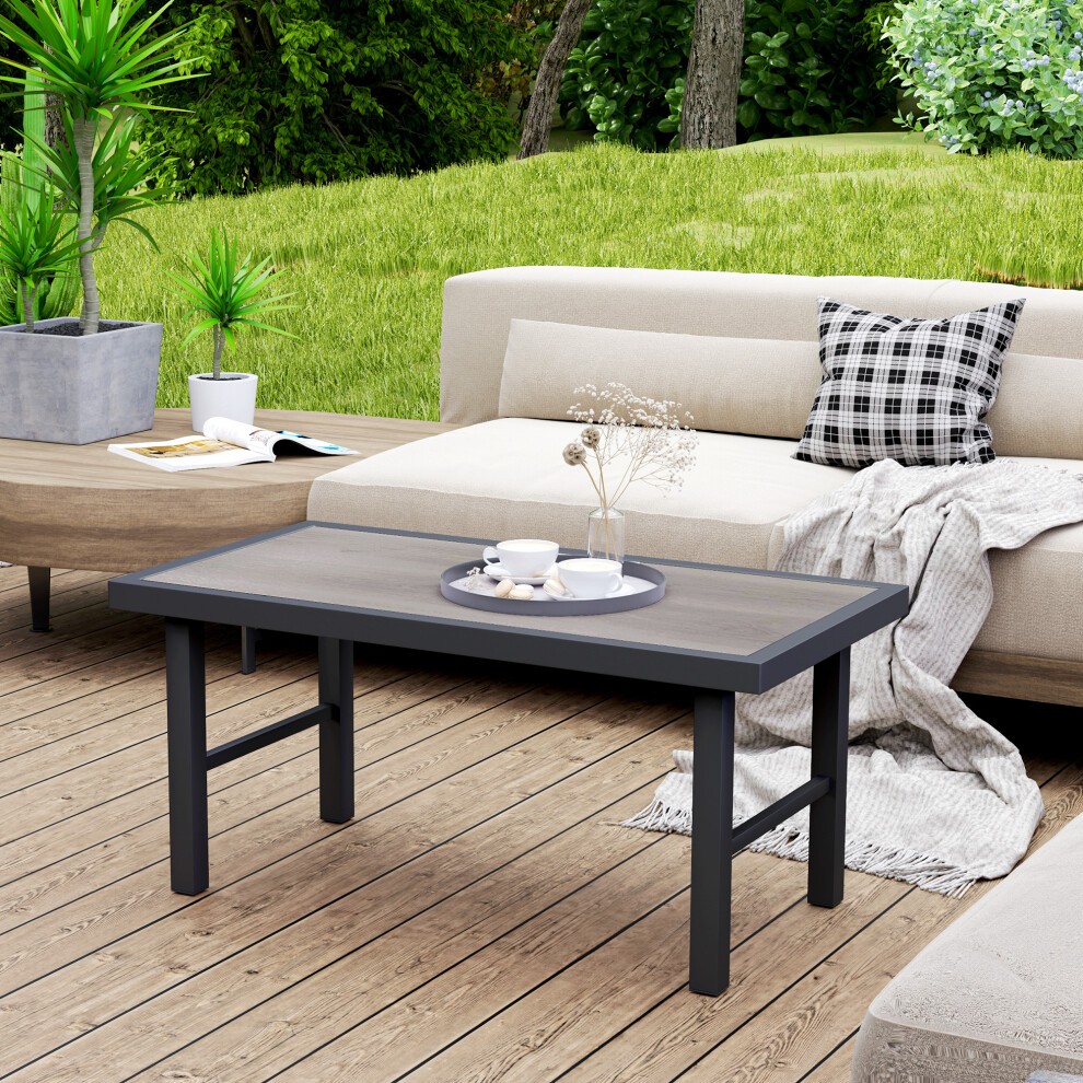 Grey wood-effect coffee table with SPC woodgrain tabletop, featuring a sturdy black frame, set on a wooden deck with a sofa and decorative plants in the background.