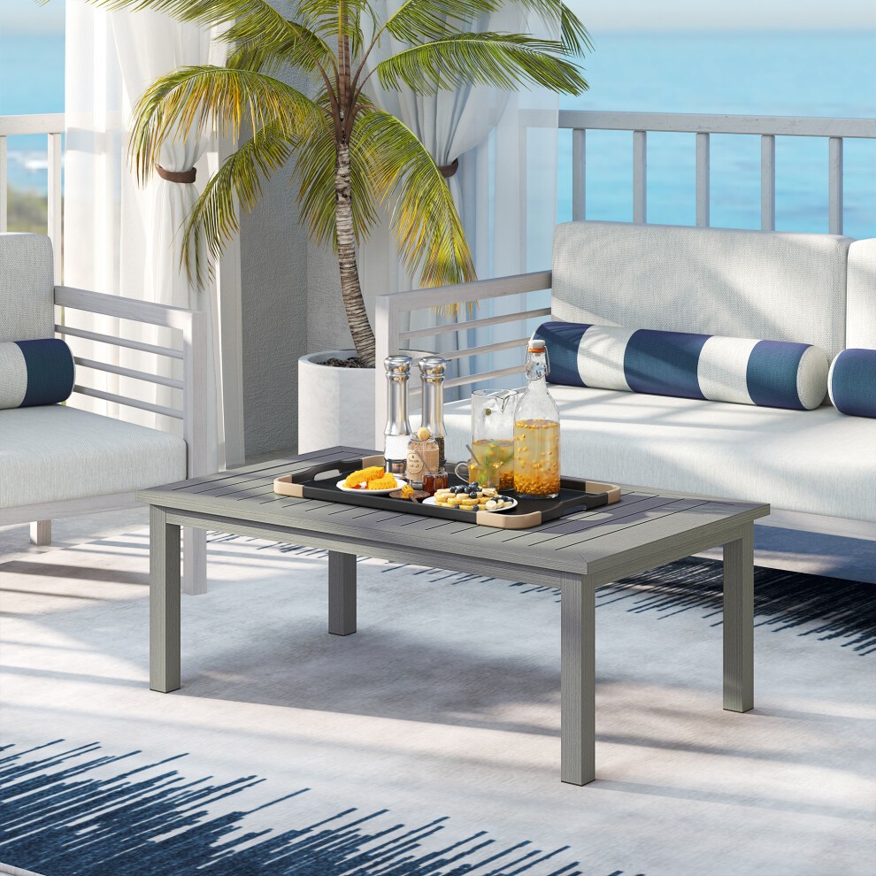 Aluminium outdoor coffee table with a grey wood grain effect, featuring a sleek design, placed on a patio with a tropical backdrop and surrounded by modern seating.