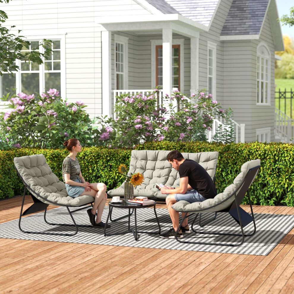 Light grey cushioned loveseat and chairs with black metal frames, accompanied by a matching table, set on a wooden patio surrounded by greenery and a house in the background.