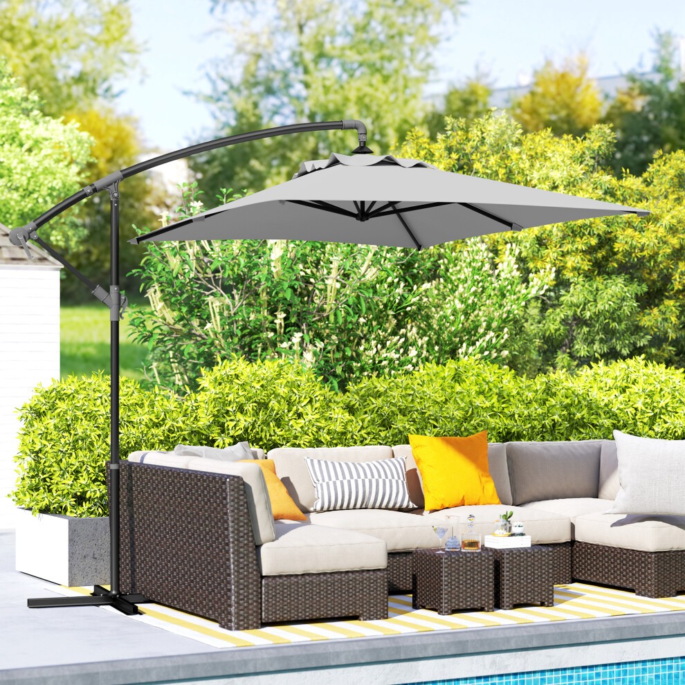 Light grey cantilever parasol with a cross base and crank handle, set beside a patio sofa with cushions, surrounded by greenery.