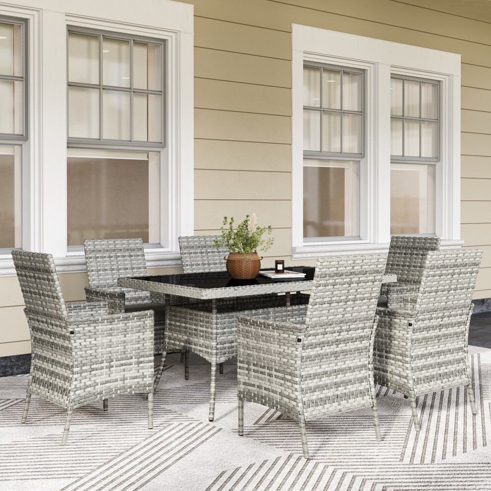 Mixed-grey rattan garden furniture set featuring a rectangular table and six cushioned chairs, set against a light-colored wall and patterned rug.