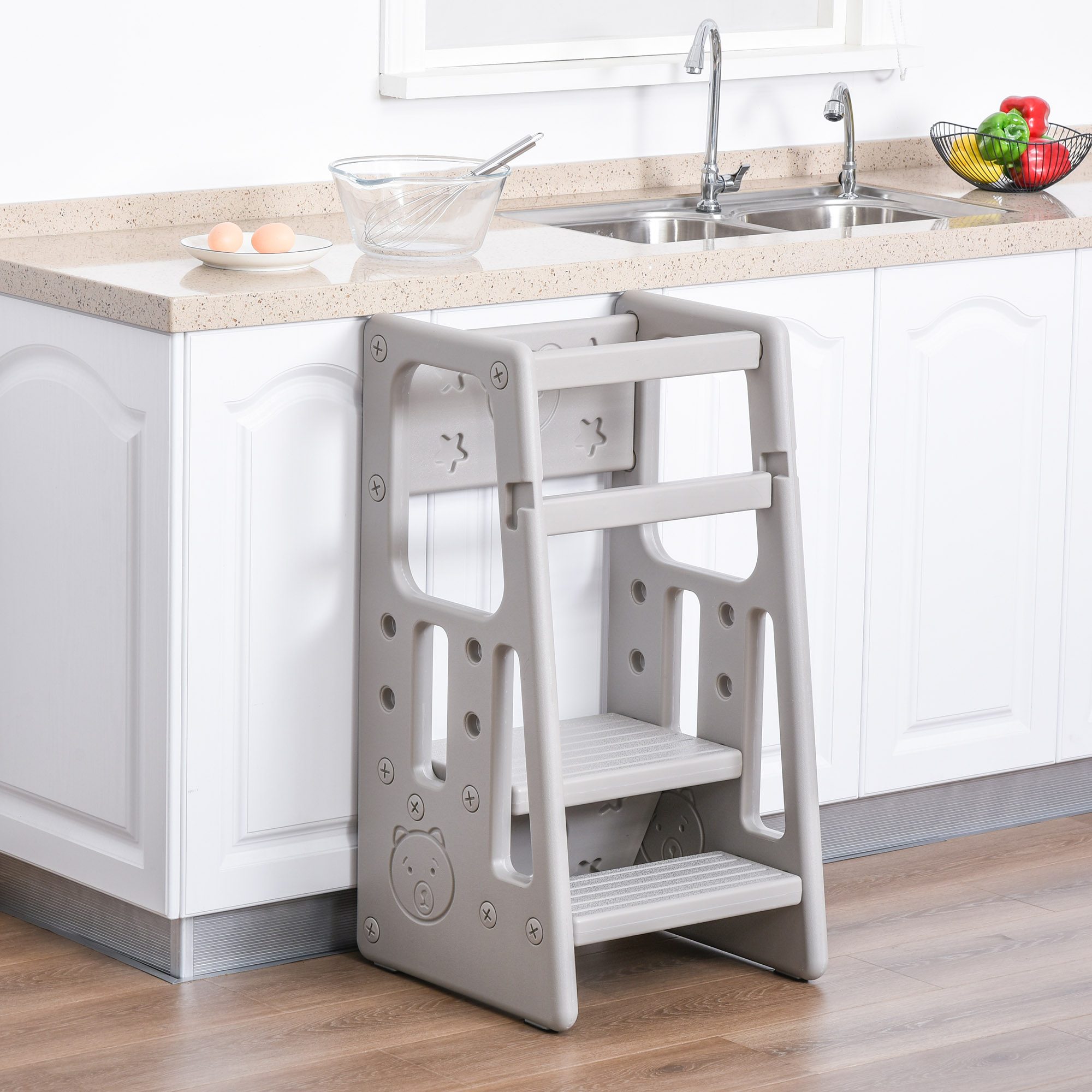 Adjustable grey kids' step stool with three heights, featuring a sturdy design, non-slip steps, and a playful bear motif, positioned near a kitchen counter with eggs and utensils.