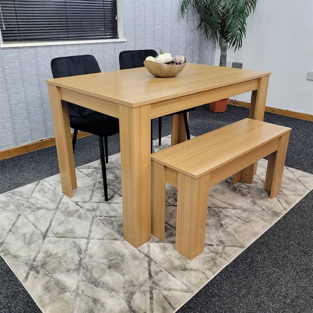 Beige KOSY KOALA dining table set featuring a rectangular table, two black chairs, and a matching bench, all set on a textured gray rug in a modern room.