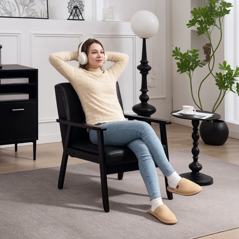 Black PU leather accent chair with armrests, featuring a modern design, paired with a small black side table and a woman wearing headphones, in a stylish living room setting.