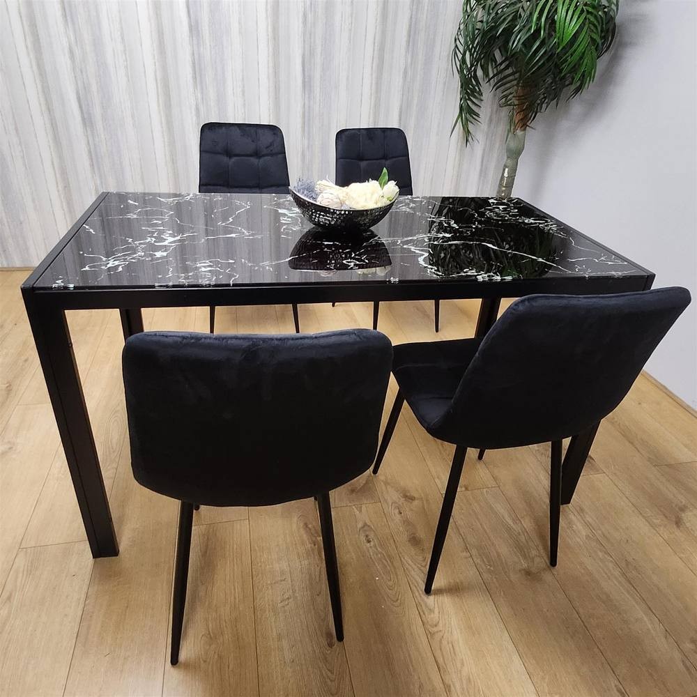 Black glass dining table with a marble effect, featuring four tufted velvet chairs in clear design, set against a light wood floor and a green plant backdrop.