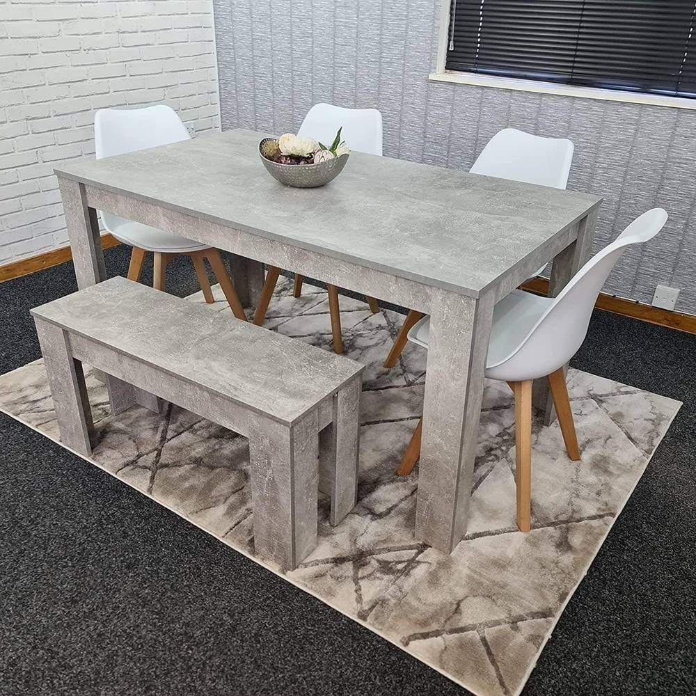 Grey dining table set featuring a rectangular table, four white chairs with wooden legs, and a matching bench, all placed on a patterned rug in a modern setting.