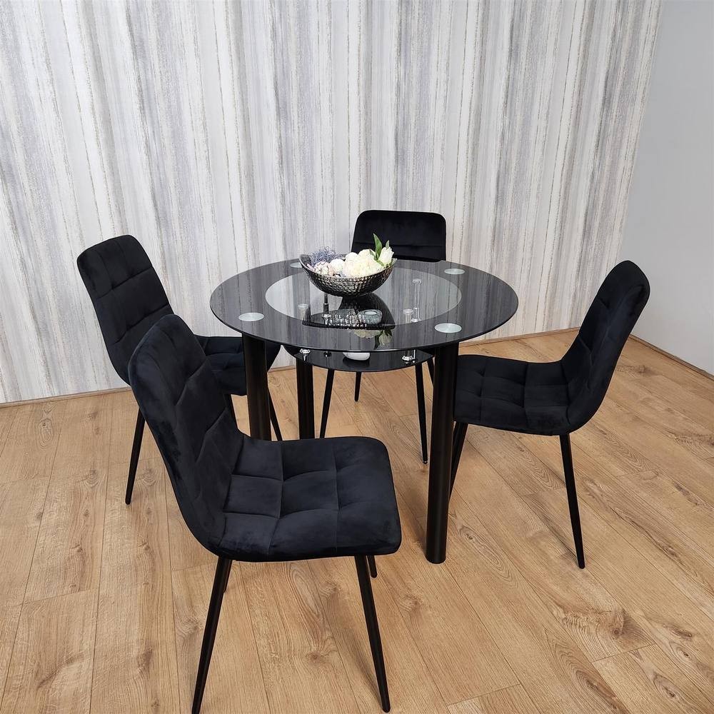 Black KOSY KOALA dining table set featuring a round glass top and four matching upholstered chairs with sleek black legs, set against a light wood floor and textured wall.