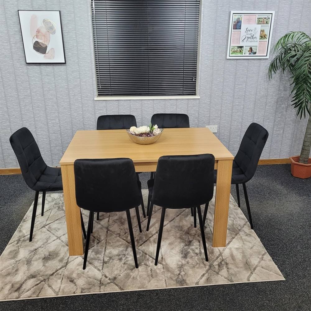 Beige dining table set featuring a rectangular wooden table with six black upholstered chairs, all set on a patterned rug in a modern dining room.