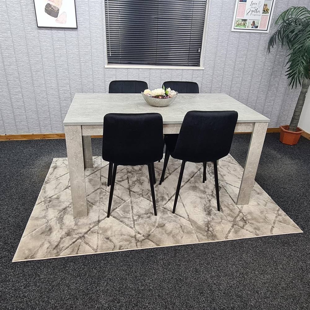 Grey KOSY KOALA dining table with four black upholstered chairs, set on a patterned rug, surrounded by a minimalist room with decorative wall art and a potted plant.
