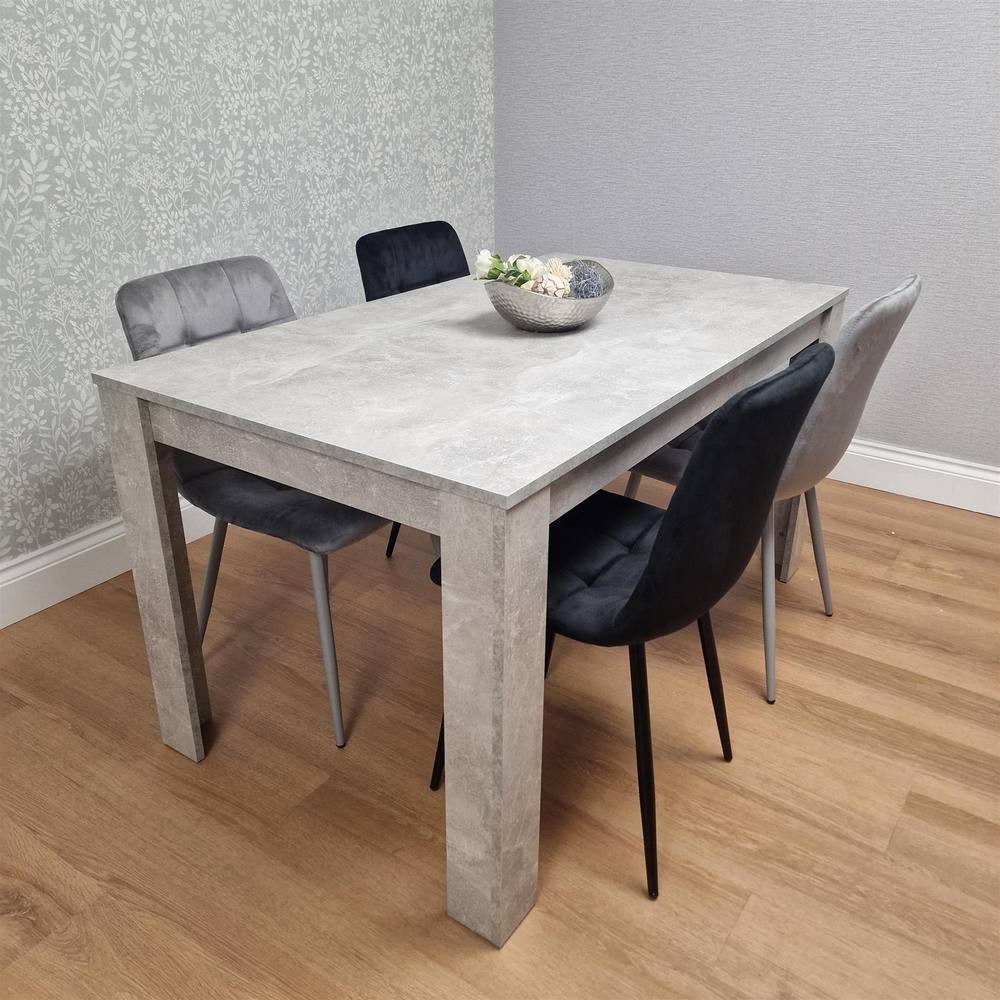 Grey dining table set featuring a rectangular stone-like tabletop and four upholstered chairs in black and grey, set against a textured light grey wall.