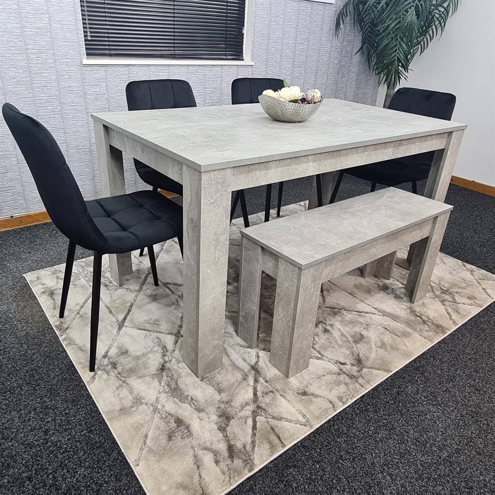 Grey dining table set featuring a rectangular table, four black upholstered chairs, and a matching bench, all on a patterned beige rug in a modern dining space.
