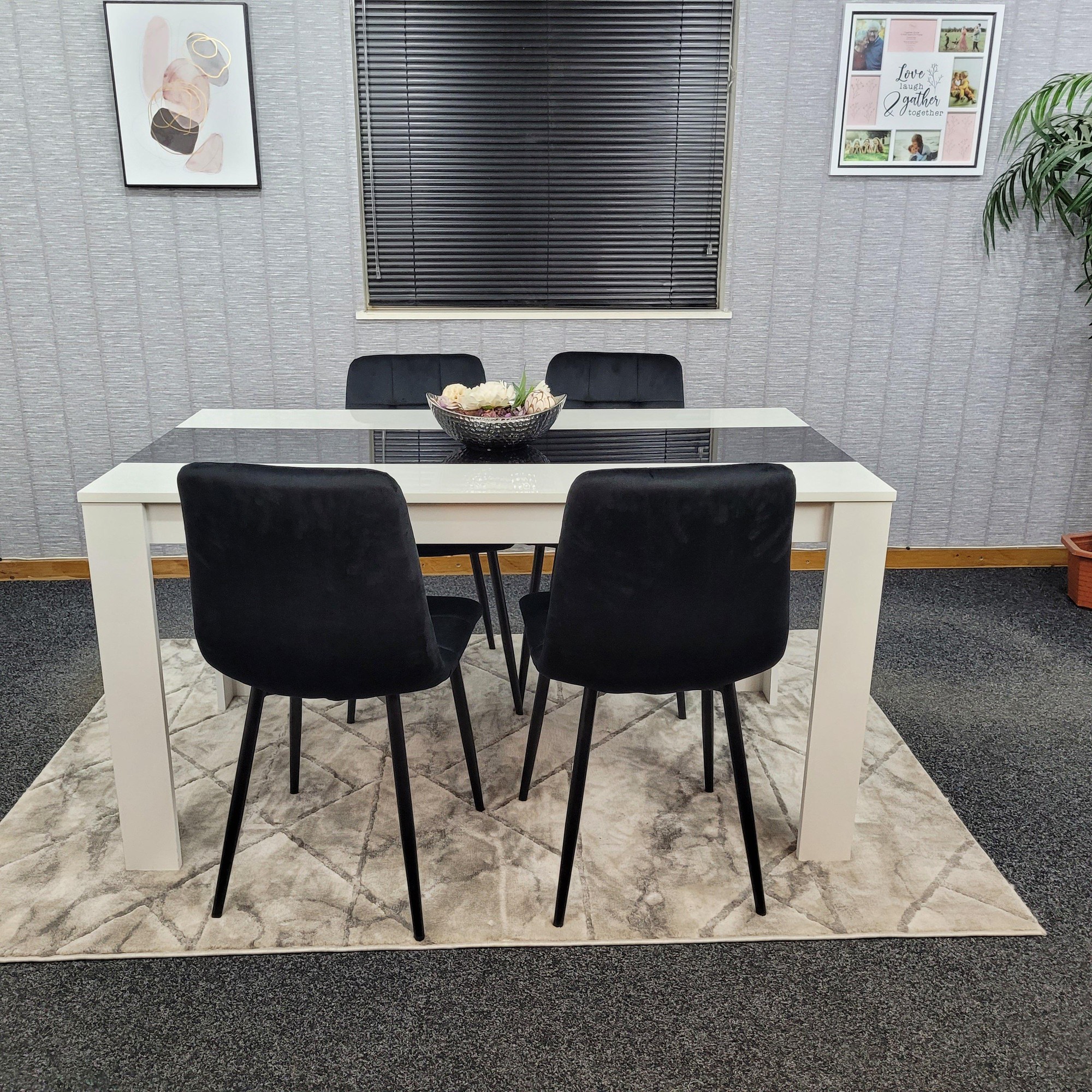 Stylish wooden dining table in white with a black top, accompanied by four tufted velvet chairs in black, set on a textured rug in a modern interior.