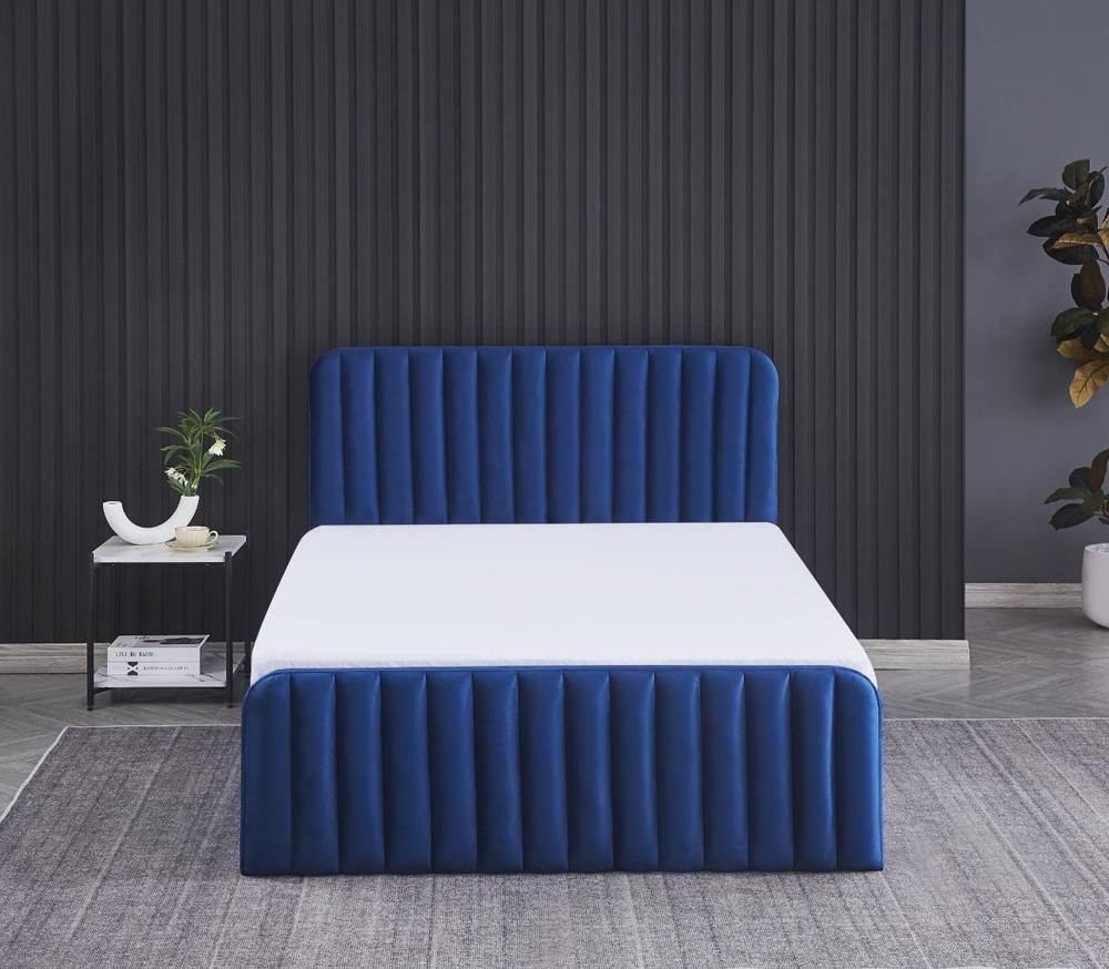 Blue velvet ottoman gas lift storage bed with a 4ft6 double frame and a white mattress, featuring vertical tufted detailing and a modern design against a dark wall.