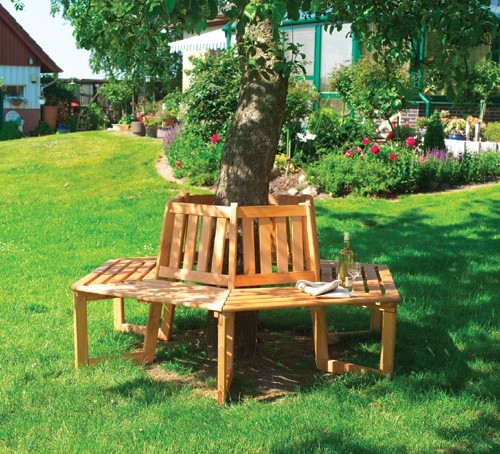 Solid brown treated wood garden tree bench with a curved design, positioned around a tree, featuring slatted seating and a natural finish, set in a lush green lawn.