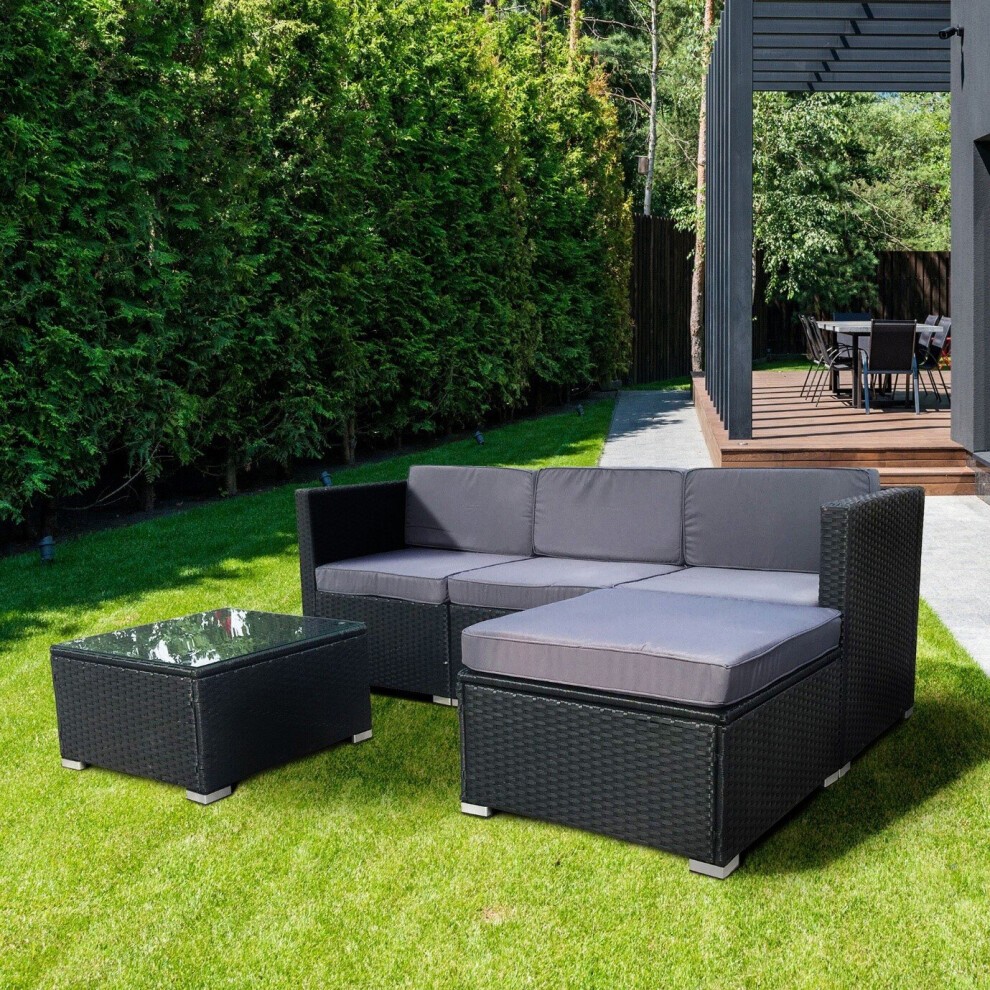 Black 5-piece MCC rattan outdoor garden furniture set featuring a sectional sofa with gray cushions and a glass-top coffee table, set on a green lawn.