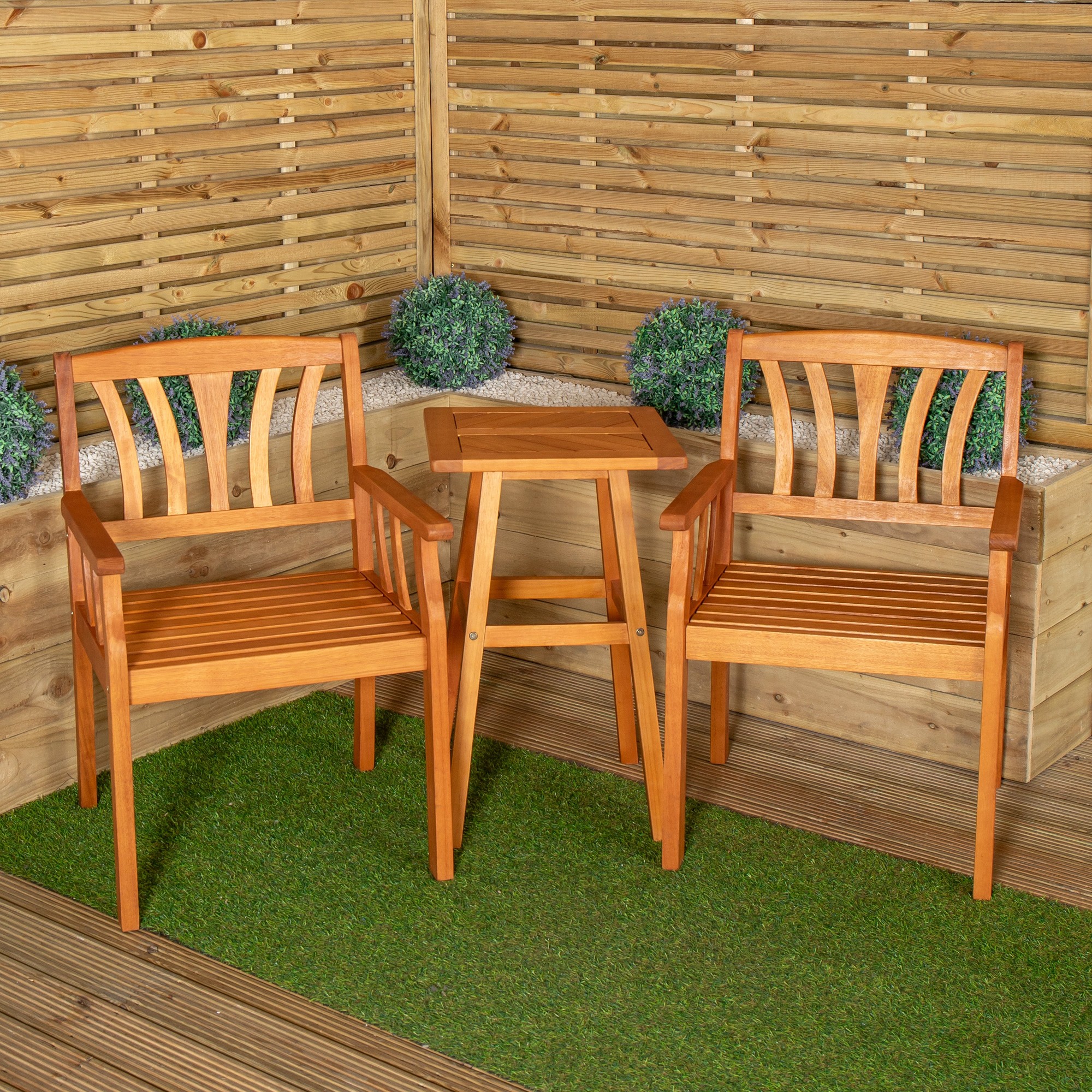 Brown wooden slatted side table with two matching chairs, featuring armrests and a natural finish, set against a wooden backdrop with potted greenery.