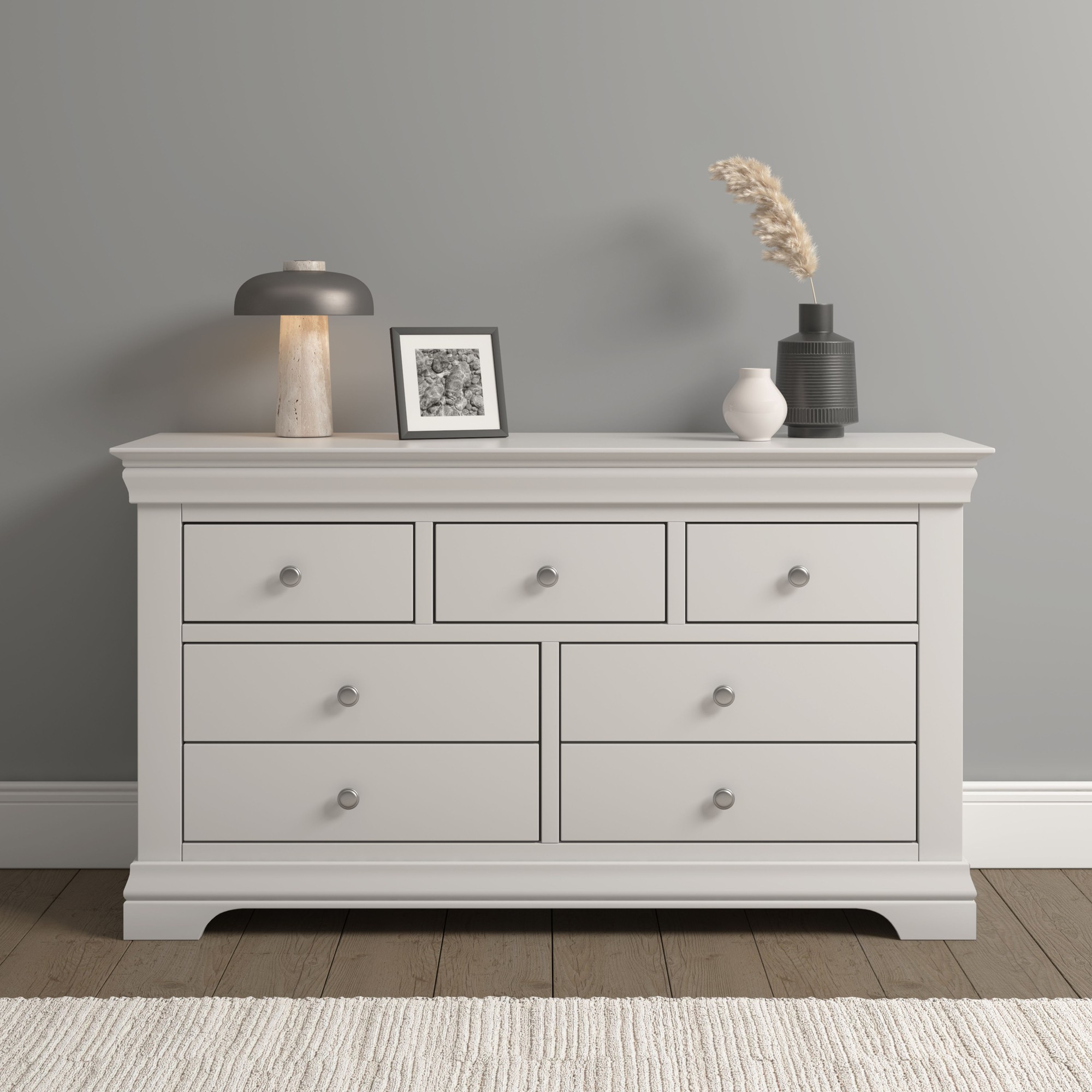 Bordeaux 3+2 drawer chest in a soft white finish, featuring six spacious drawers with round silver knobs, set against a neutral wall with decorative items on top.