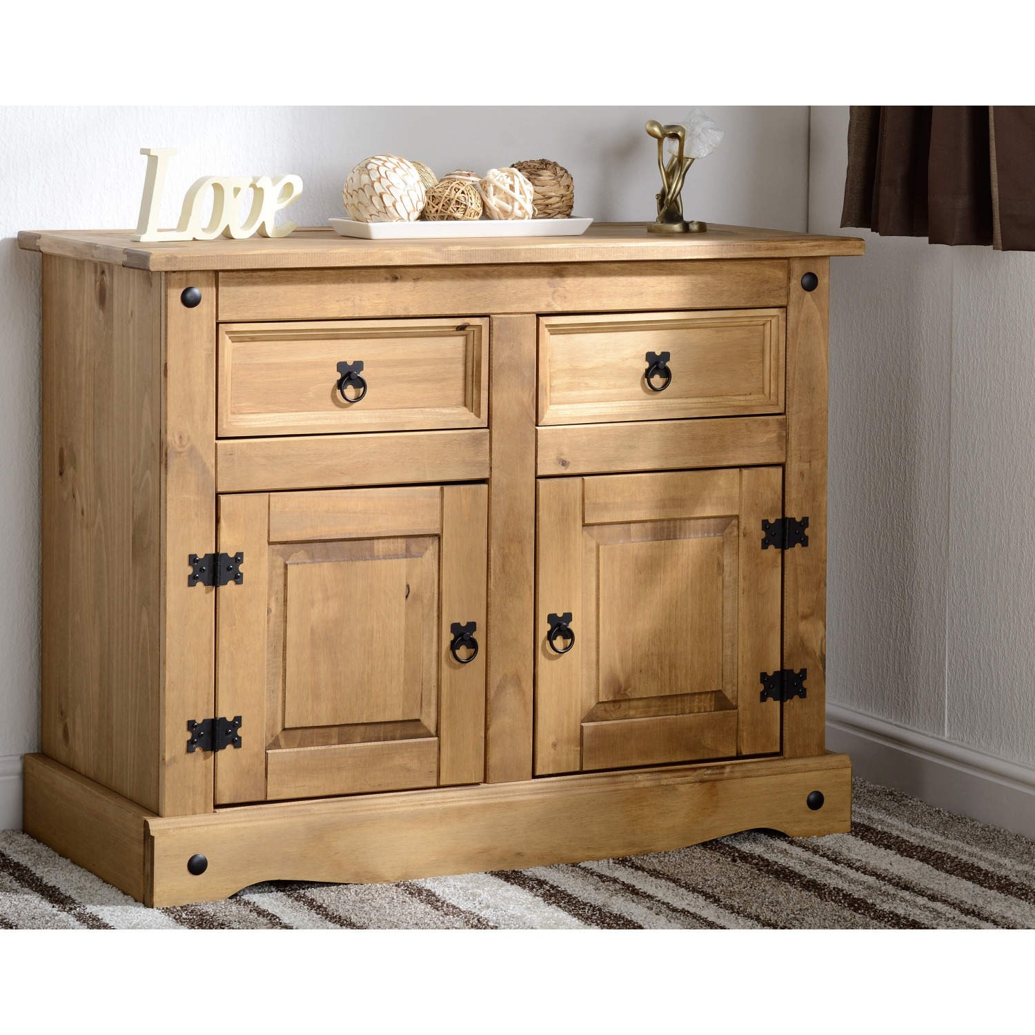 Distressed waxed pine sideboard in brown featuring two doors, two drawers, and black metal handles, complemented by decorative accents on the corners.