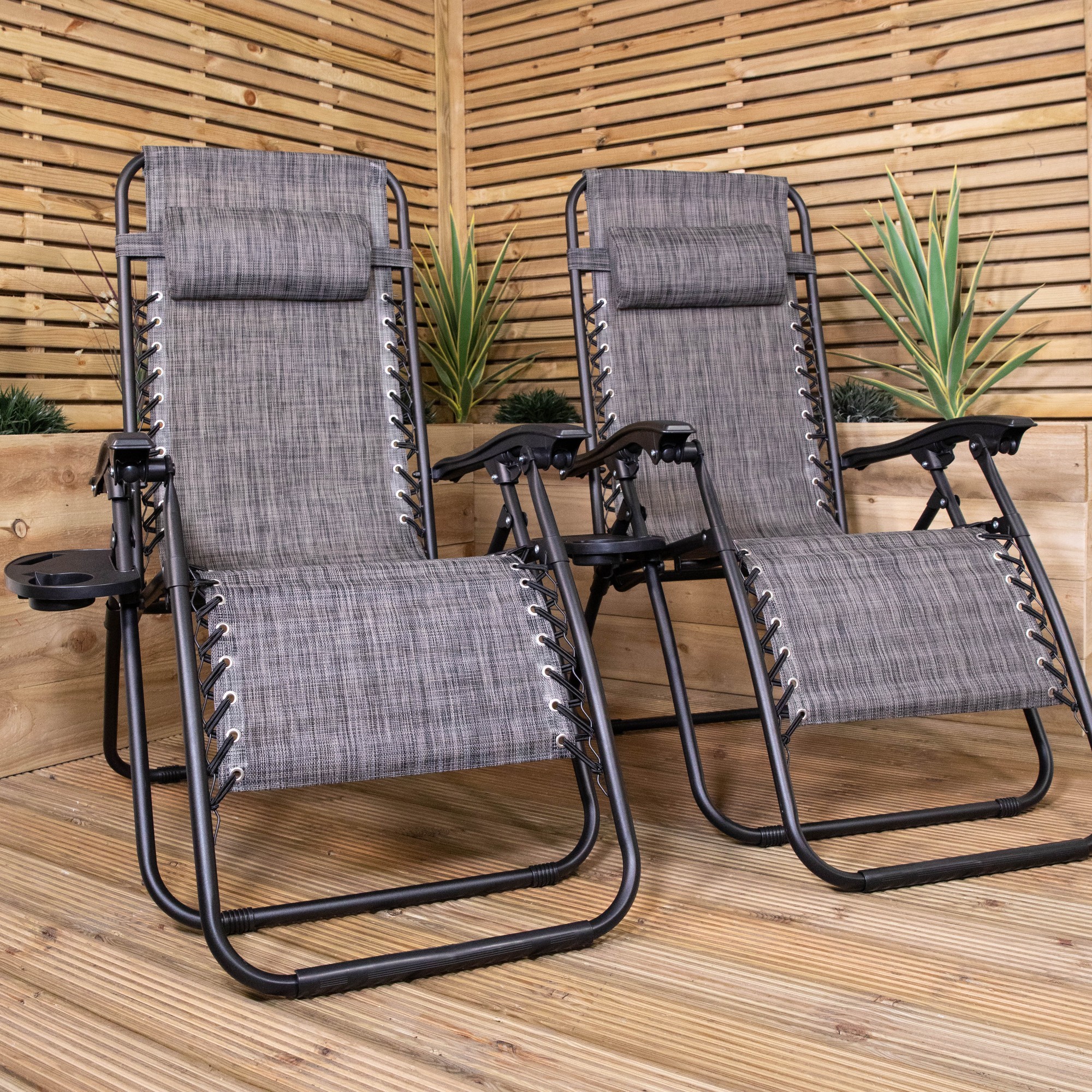 Set of 2 multi-position zero gravity relaxer chairs in mixed grey, featuring a sturdy metal frame, adjustable headrests, and cup holders, set against a wooden backdrop with greenery.