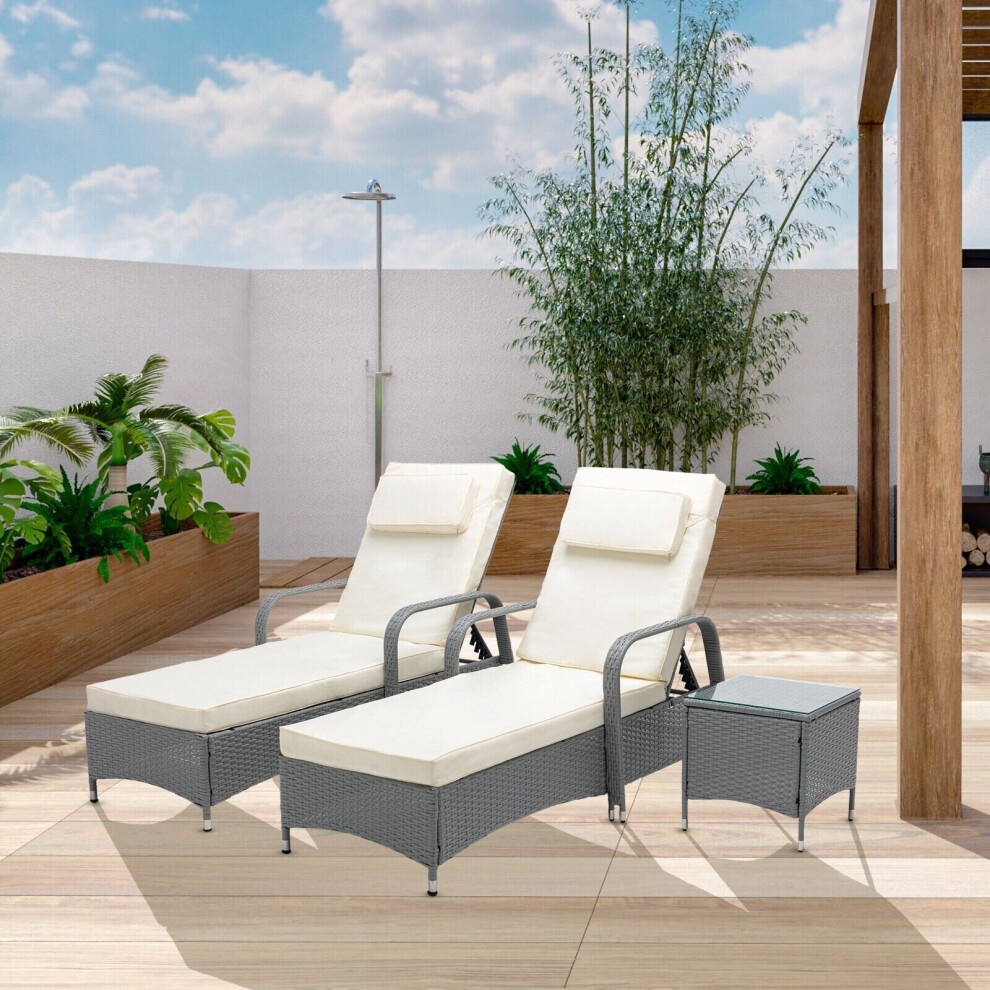 Grey rattan sun lounger bed recliner set with cream cushions, featuring two loungers with adjustable backs and a small side table, set against a sunny outdoor backdrop.