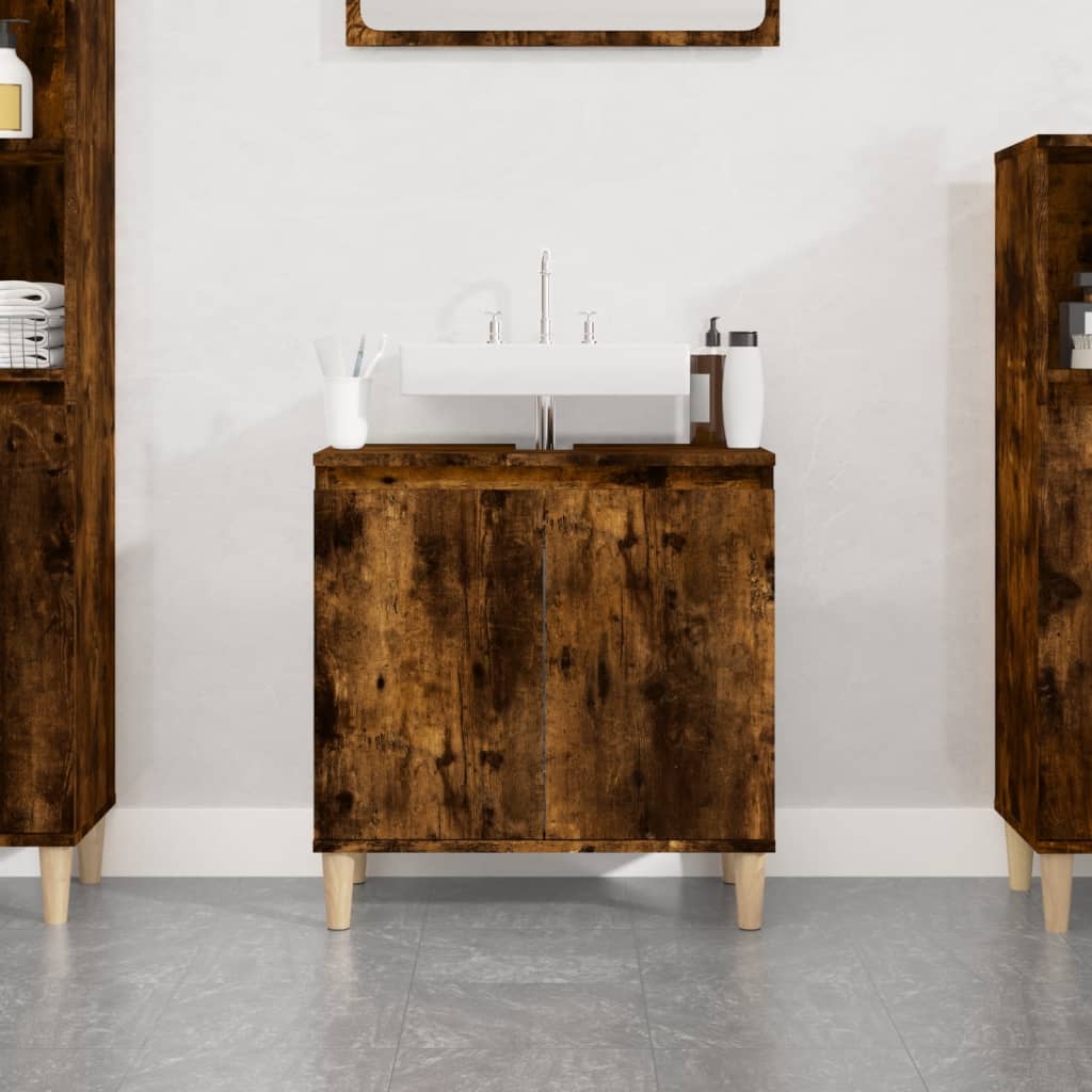 Smoked oak sink cabinet with a minimalist design, featuring two doors, a white sink on top, and light wooden legs, set against a neutral wall.