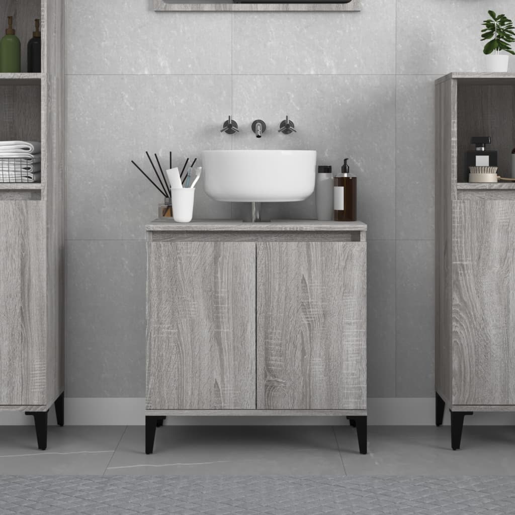 Grey Sonoma sink cabinet made of engineered wood, featuring two doors, a countertop with a white sink, and black legs, set against a light grey tiled wall.