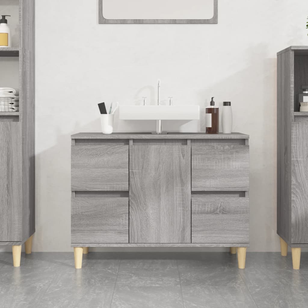 Grey Sonoma sink cabinet made of engineered wood, featuring four drawers and two doors, complemented by light wooden legs, with a white sink on top.
