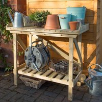 Wooden potting bench with slatted shelf, side supports, and various gardening tools and pots on top.