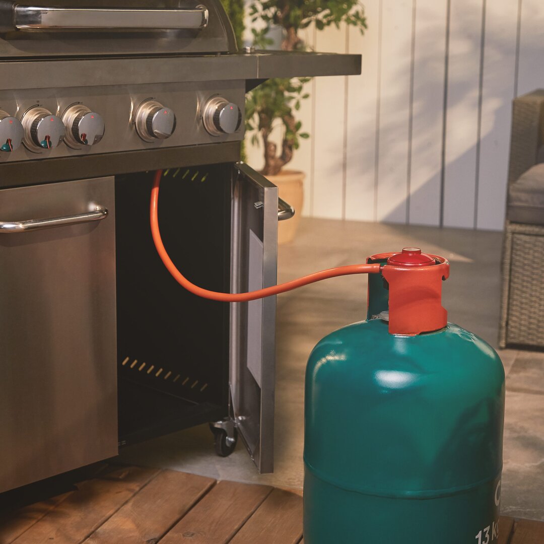 27mm quick connect propane regulator in orange, attached to a green propane tank, positioned near a stainless steel grill with knobs, set in a patio environment.