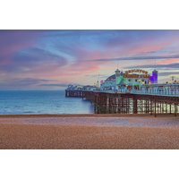 Brighton Pier at sunset with colorful lights, sandy beach, and calm sea, promoting Maldron Hotel Brighton City Centre.