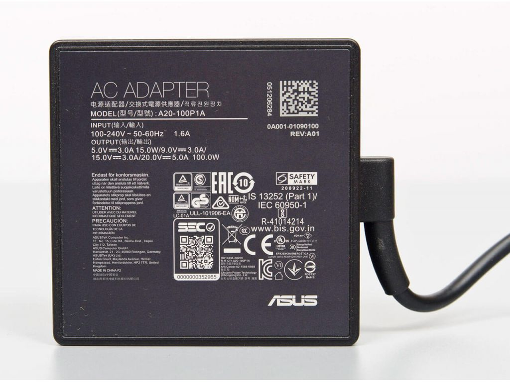 Black ASUS power adapter with a square design, featuring input/output specifications and safety information printed on the surface, and a black power cord attached.