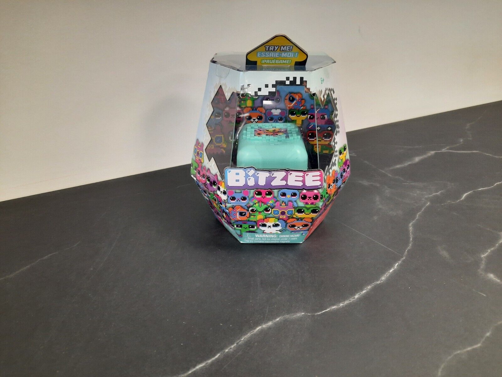 Mint-colored hexagonal packaging featuring various colorful digital pets, with a transparent top showcasing the interactive pet inside and vibrant graphics on the front.