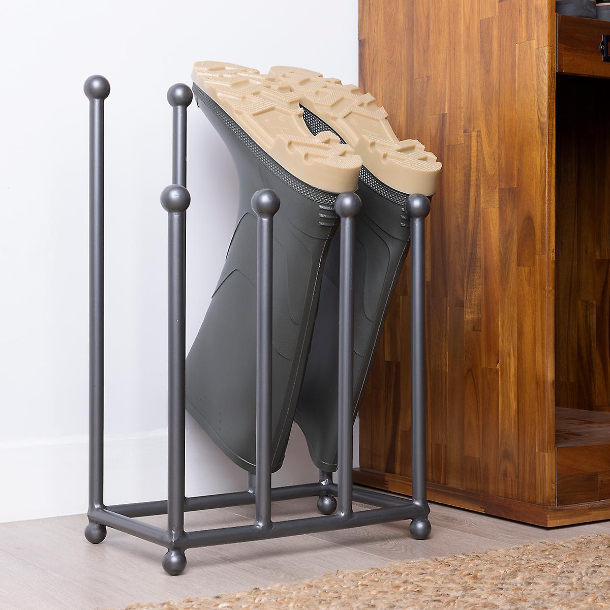 Grey iron boot stand with four vertical rods and rounded tops, holding a pair of black rubber boots with tan soles, positioned against a wooden surface.