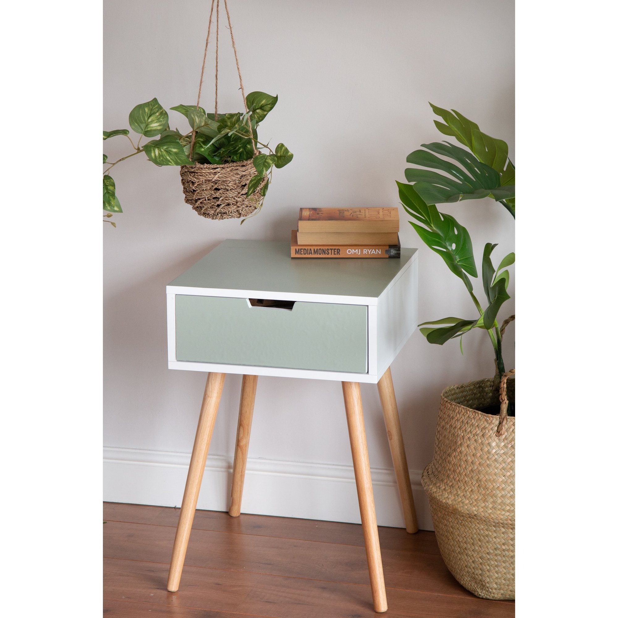 Matte sage green sticky back plastic roll by d-c-fix, measuring 67.5cm x 2m, displayed on a stylish nightstand with wooden legs and plants in the background.