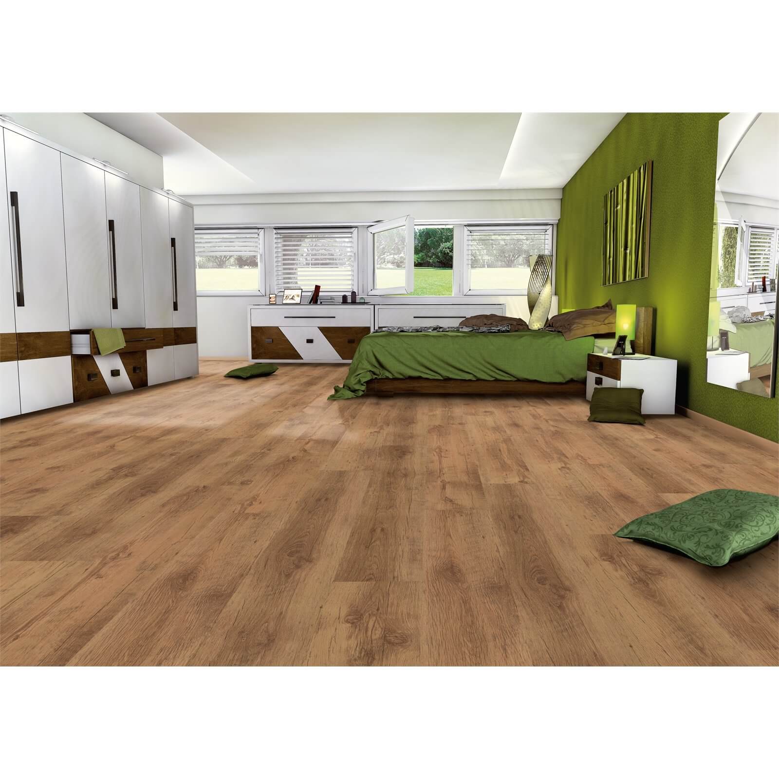 Beaumont Oak laminate flooring in warm oak tones, featuring a smooth surface and natural wood grain texture, displayed in a modern bedroom setting with green accents.